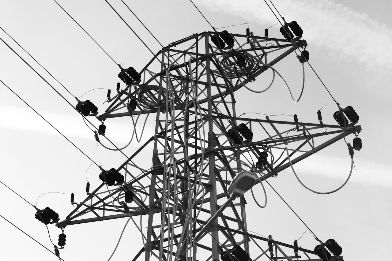 A black and white photo featuring a power line tower with cables against a clear sky.