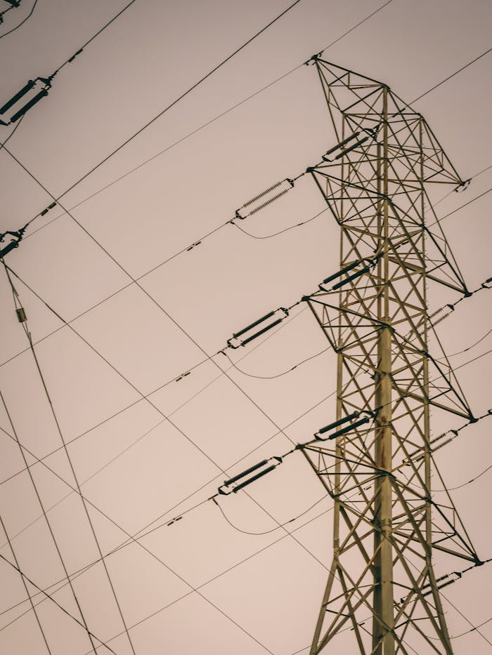 A low angle shot of a high voltage transmission tower with steel trusses and power lines.